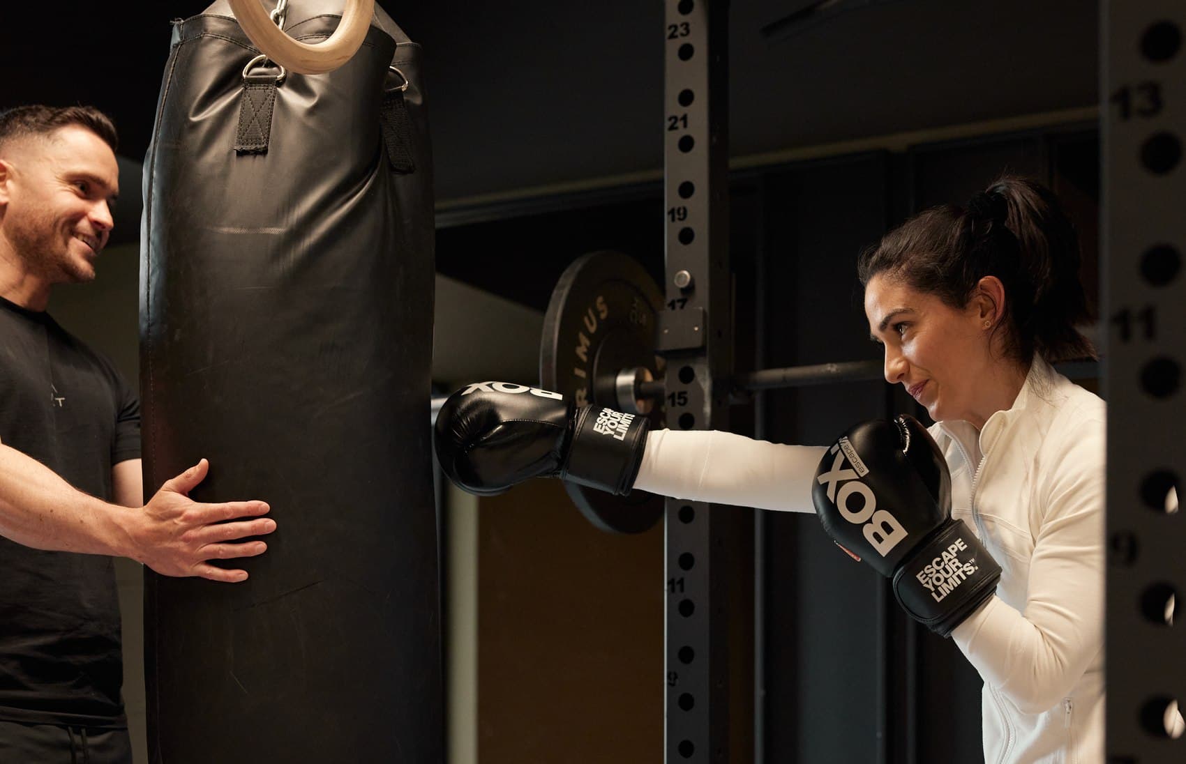 An ALT RESIDE coach steadying a heavy bag while a resident works through a boxing round