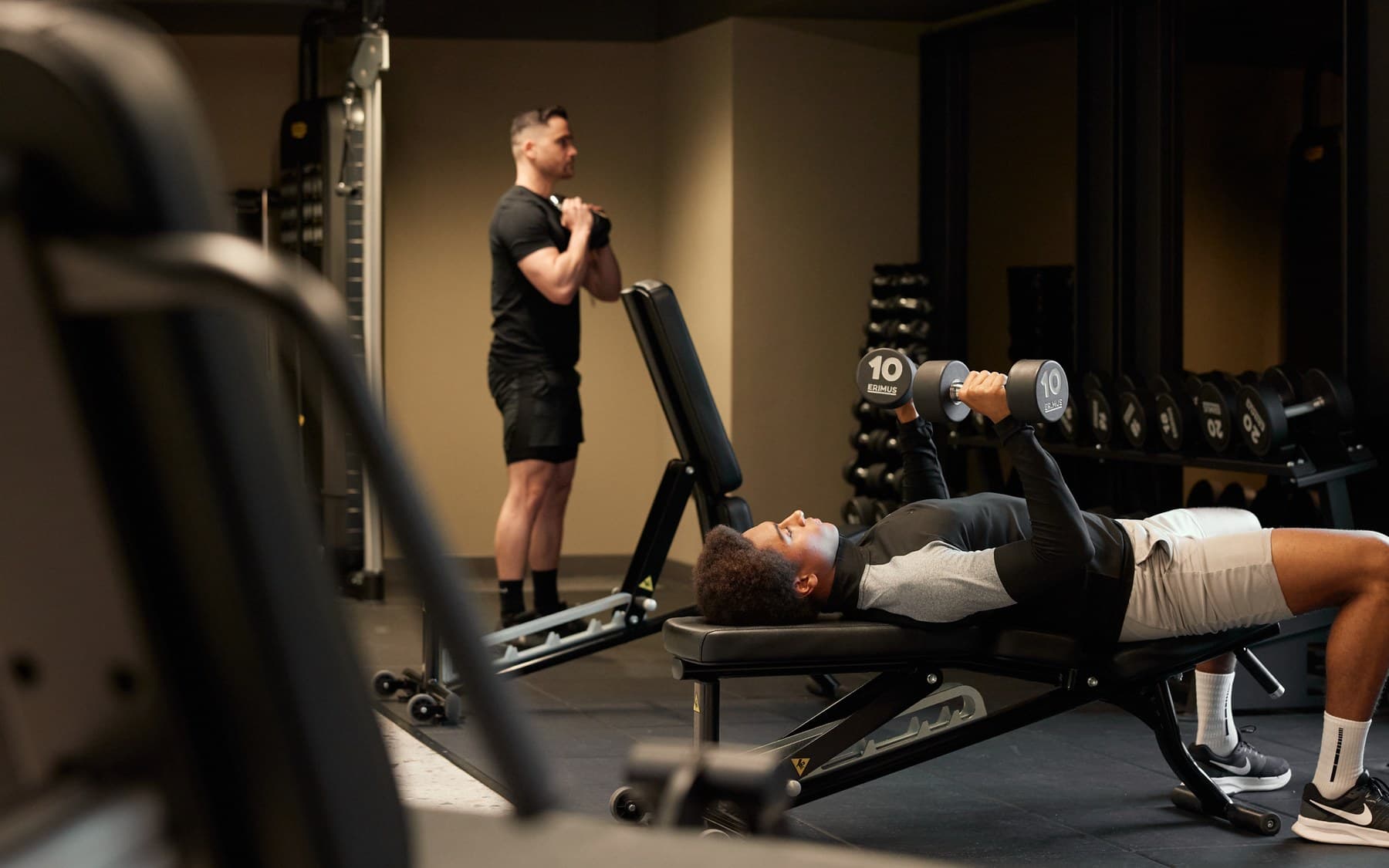 An ALT RESIDE coach spotting a resident on a dumbbell press