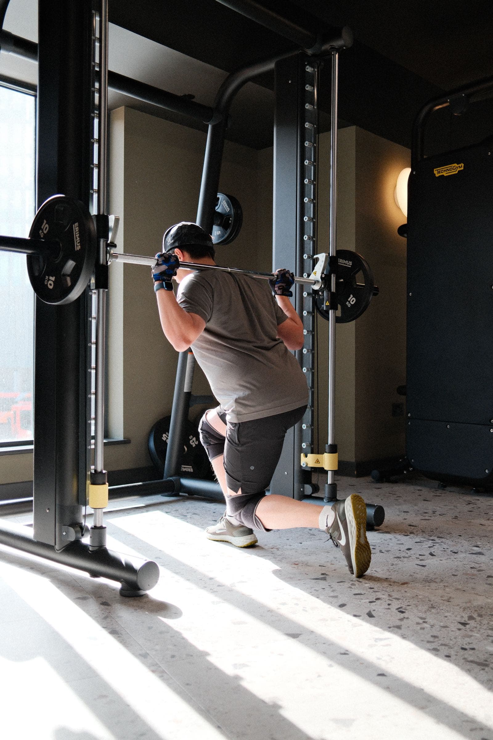 A resident squatting under a barbell in the rack, sunlight across the gym floor