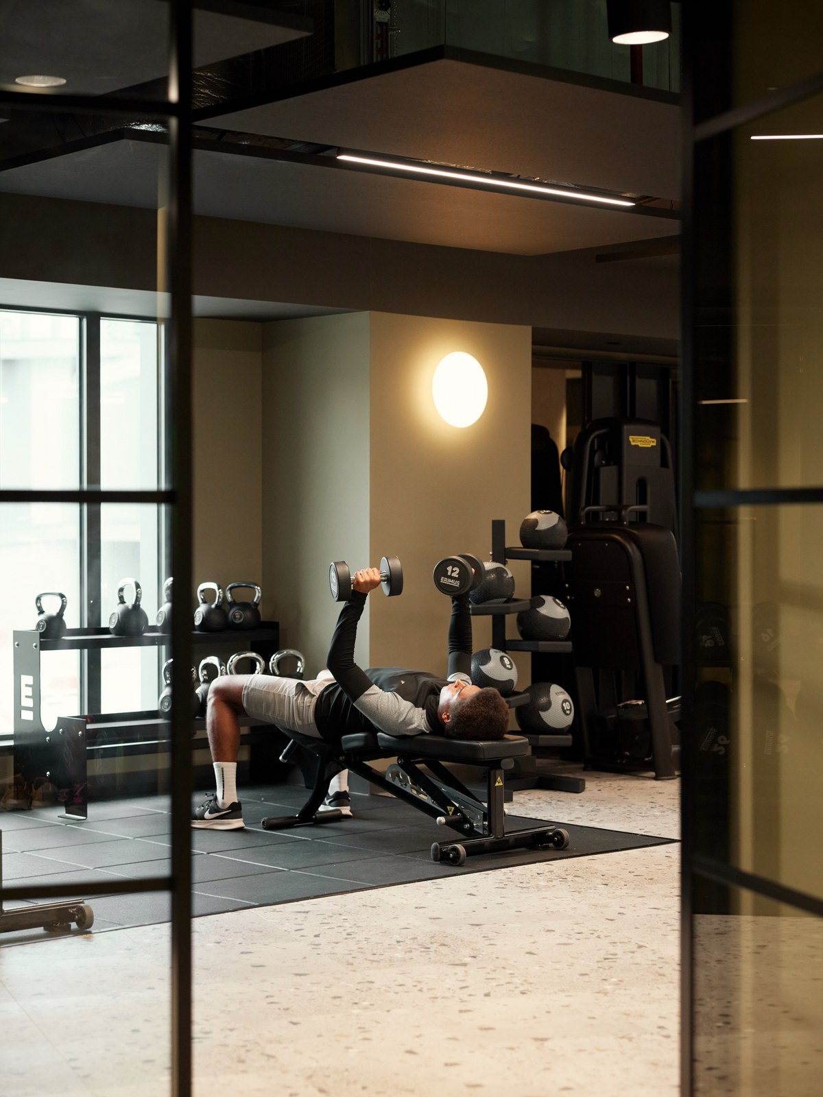 A resident training with dumbbells in an ALT RESIDE residents' gym, seen through the glass doorway